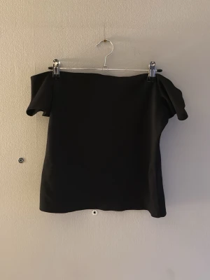 Svart offshoulder topp - Säljer en stilren svart offshoulder topp med korta ärmar. Toppen har en enkel och elegant design som passar perfekt till många olika outfits. Materialet känns mjukt och följsamt mot huden.