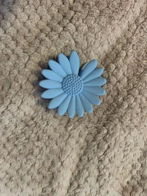 Blå hårklämma i form av blomma - Söt hårklämma i ljusblå plast formad som en blomma med detaljerade kronblad och prickig mitt. Perfekt för att piffa upp frisyren med en lekfull och trendig accessoar. Klämman har ett stadigt grepp och passar till många olika hårstilar.