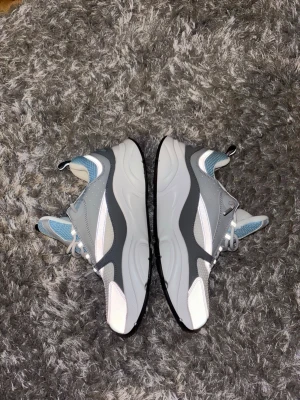Grå och vita chunky sneakers - Snygga chunky sneakers i grått, vitt och ljusblått med detaljer i mesh och syntet. Skorna har en tjock sula och cool design med flera lager material. Perfekta för dig som gillar streetwear och vill sticka ut med dina skor.