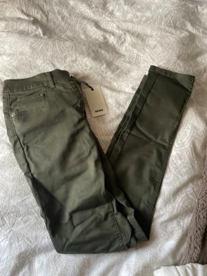 Olivgröna jeans från BikBok - Säljer ett par olivgröna jeans från BikBok i storlek M. Jeansen har smal passform, klassiska fem fickor och silverfärgade nitar. Materialet är mjukt och stretchigt för extra komfort.
