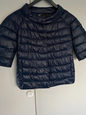 Mörkblå Trekvartärmar dunväst - Snygg mörkblå Trekvartärmar dunväst med korta ärmar och bred krage. Västen har en quiltad design med horisontella sömmar och stängs framtill. Perfekt för lager på lager och ger en modern look till din outfit. Obs👀Jag rekommenderar storlek XS och XXS 👌!!