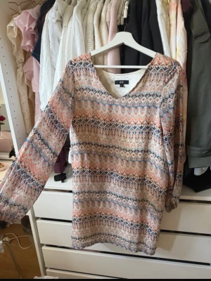 Mönstrad långärmad klänning Dry Lake - Säljer en snygg långärmad klänning från Dry Lake i storlek XS. Klänningen har ett färgglatt etnoinspirerat mönster i beige, blått, orange och vitt samt v-ringning. Materialet känns lätt och flowy, perfekt för dig som gillar boho-vibbar.