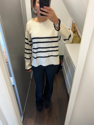 Randig stickad tröja Vero Moda - Säljer en krämvit stickad tröja från Vero Moda med svarta horisontella ränder. Tröjan har rund halsringning, långa ärmar och ribbade muddar. Perfekt för en avslappnad och trendig look.
