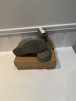 Gråa UGG Classic Mini boots - UGG Classic Mini boots i grå mocka med mjukt foder och robust sula. Skorna är i nyskick bara använda ett fåtal gånger då dem växtes ur snabbt. Perfekt för dig som vill ha ett par riktigt fina skor till kallare väder men inte spendera 2399 som dem köpte för. Medans jag säljer dem för 1100. Kan även tänka mig gå ner till 800 vid en snabb affär.