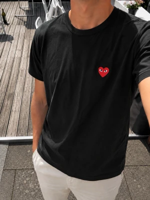 Comme des Garçons PLAY T-shirt Svart – Red Heart Logo – Strl M - Snygg och stilren Comme des Garçons PLAY T-shirt i svart med det ikoniska röda Heart-logoet med ögon på bröstet.  En klassisk modell med rund hals och korta ärmar. Enkel att matcha och passar perfekt till både jeans, chinos och shorts.  * Comme des Garçons PLAY * Svart * Rött Heart-logo med ögon * Kort ärm * Rund hals * Storlek M * 100% bomull * Klassisk och tidlös modell  Storlek: M. PLAY T-shirts kan upplevas något mindre i storleken.
