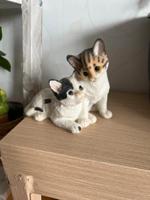 Söt kattprydnad i keramik - Dekorativ prydnad med två katteri i keramik. Ena katten sitter och den andra ligger tätt intill, båda i vita och gråbruna toner med fina detaljerade ansikten. Perfekt som gullig inredningsdetalj för kattälskare.