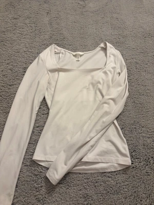 Vit långärmad topp från H&M - Säljer en enkel och stilren vit långärmad topp från H&M. Toppen har en fyrkantig ringning och är figurnära i modellen. Perfekt att matcha med jeans eller kjol för en clean look.