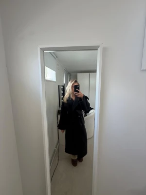 Lång svart kappa - Kappan är från Nelly med originalpris på 1000kr. Det finns tecken på användning då den är nopprig o saknar båda knapparna på båda ärmarna. ❤️