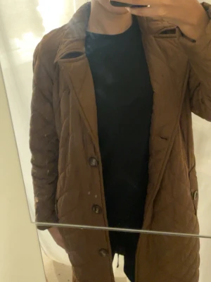 Brun quiltad lång kappa - Brun quiltad kappa med knappar framtill och klassisk krage. 