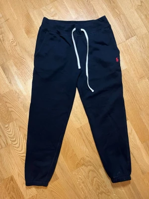 Svarta mjukisbyxor Polo Ralph Lauren - Säljer dessa snygga svarta mjukisbyxor från Polo Ralph Lauren i storlek S med röd broderad logga på vänster sida. Byxorna har vita dragsnören i midjan, muddar vid bensluten och är tillverkade i mjukt bomullsmaterial. Perfekta för chill dagar eller när du vill vara bekväm. Vid frågor, extra bilder eller liknande är det bara att kontakta mig!
