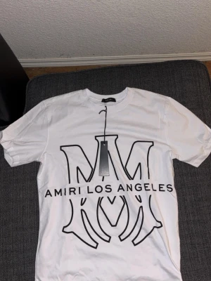 Vit Amiri t-shirt med stor logga - Säljer en vit t-shirt från Amiri med stor svart loga. Mycket fin och stilig passar bra med jeans. Aldrig använd köpte den i fel storlek. 