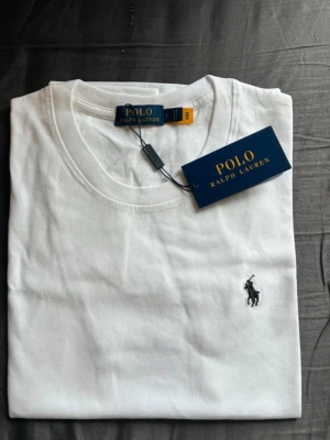  Polo T-shirt  - Klassisk vit t-shirt från Polo Ralph Lauren med rund halsringning och den ikoniska broderade loggan på bröstet. Tillverkad i mjuk bomull för en skön känsla och perfekt passform. Enkel och stilren design som funkar till allt.