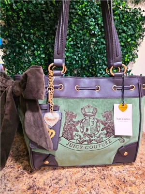 Grön handväska Juicy Couture daydreamer  - Stilren grön handväska från Juicy Couture i mocka och läderdetaljer. Väskan har stora bruna handtag, dekorativ rosett i sammet på sidan och guldfärgade metalldetaljer. Framsidan pryds av Juicy Coutures klassiska logga och en hjärtformad nyckelring.