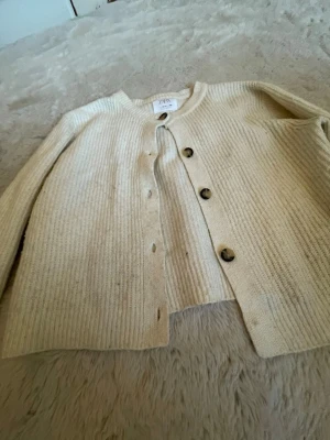 Beige ribbad kofta från Zara - Snygg beige ribbad kofta från Zara med rund halsringning och stora bruna knappar framtill.  Den är ganska så nopprig därav priset! Pris kan diskuteras och skriv för fler bilder! Koftan är i storlek 164/xs