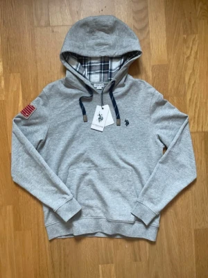 US Polo Assn. Hoodie Grå M – Ny med tags, rutig luva - Klassisk och stilren US Polo Assn. hoodie i grått med snygg rutig insida i luvan. Helt ny med lapparna kvar och aldrig använd. En tidlös modell med fina detaljer som passar perfekt till en clean och avslappnad stil. ✔️ Helt ny med lapparna kvar ✔️ Storlek M ✔️ US Polo Assn.-detaljer ✔️ Snygg flaggdetalj på ärmen ✔️ Mjuk och skön kvalitet 📦 Vill du köpa flera av mina annonser kan jag självklart skicka dem tillsammans! Paketpris kan ordnas vid köp av flera. Alltid öppen för bud! 📩 Skickas snabbt!