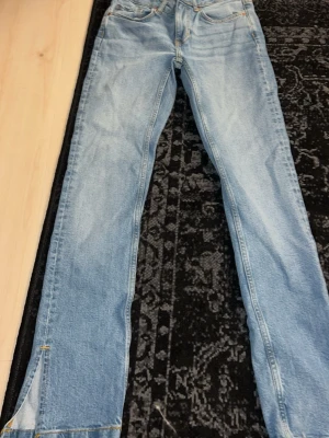 Ljusblå raka jeans med slits - Säljer ett par ljusblå jeans med raka ben och slitsdetalj längst ner på benen. Använt ett fåtal gånger.