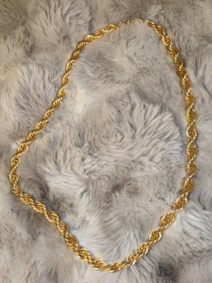 Guldfärgat tvinnat halsband - Snyggt halsband i guldpläterad metall med tvinnad kedja som ger en chunky och trendig look. Perfekt för att lyfta vilken outfit som helst med sin glansiga finish och unika design. Lås med enkel ringöppning.