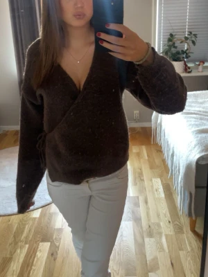 Brun stickad kofta - Säljer en mörkbrun stickade tröjan med knytband i sidan. Tröjan har djup v-ringning och långa ärmar. Perfekt för dig som gillar en avslappnad men ändå trendig look. Materialet ser mjukt och lite fluffigt ut.