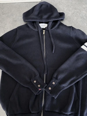 Marinblå hoodie från Thom Browne - Heinzt! Nu säljer jag denna feta marinblåa stickade zip-hoodien från Thom Browne. Den är sparsamt använd och i väldigt bra skick! Skriv gärna vid frågor eller intresse.