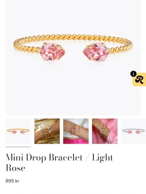 Guldarmband med rosa stenar - Säljer ett snyggt armband i guldton med tvinnad design och två stora ljusrosa droppformade stenar i ändarna. Perfekt för dig som vill ha något som sticker ut och ger en lyxig touch till din stil.