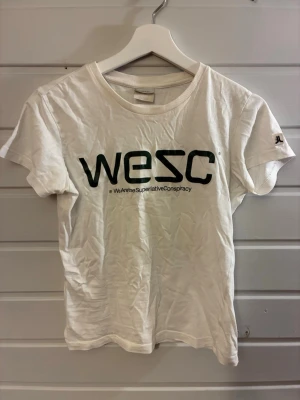 Vit t-shirt från WESC med tryck - Vit t-shirt från WESC med svart logotyptryck på bröstet och rund hals. Klassisk passform och korta ärmar. Perfekt till jeans eller shorts för en avslappnad look.