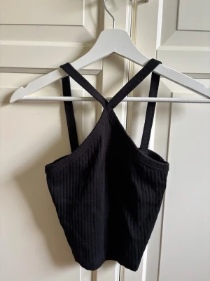 Svart ribbad linnetopp Gina Tricot - Säljer en svart ribbad linnetopp från Gina Tricot i storlek XS. Toppen har smala axelband som korsas där fram och övergår till rakaband i ryggen.  Tröjan är tillverkad i ett mjukt, stretchigt material. Perfekt att matcha med jeans eller kjol för en trendig look.
