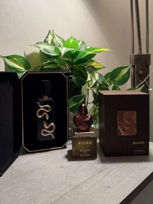 Parfym - Två lyxiga parfymer: Veneno från French Avenue i svart flaska med guldig ormdekor och Muharib Maison i fyrkantig guldbrun flaska med bronsfärgad byst på korken. Båda kommer i eleganta förpackningar och har en exklusiv design som sticker ut i parfymhyllan.