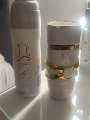 Yara parfym och deo spray från Lattafa - Säljer ett set med Yara parfym och matchande deo spray från Lattafa. Båda har en elegant ljuslila färg med guldiga detaljer och arabiska inskriptioner. Parfymflaskan har en unik form med guldband runt och sprayen är cylinderformad. Perfekt för dig som gillar lyxiga dofter. De är använda 2 ggr det är helt fullt i båda 