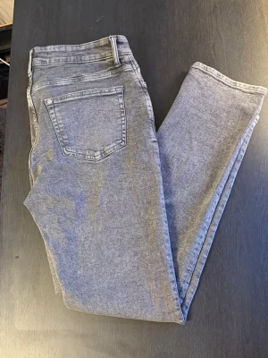 Grå slim fit jeans med hög midja - Säljer ett par grå slim fit jeans med hög midja och klassisk femficksdesign. Jeansen har en tvättad look och raka ben som smalnar av. Perfekta till vardags för en avslappnad men ändå snygg stil.