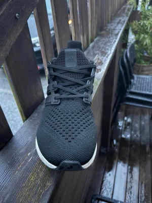Ultraboost Adidas  - Snygga svarta Adidas sneakers med ventilerande mesh-ovandel och klassiska tre ränder på sidan. Skon har en vit, dämpad sula och svarta skosnören. Perfekt för dig som gillar stilrena och bekväma sneakers med sportig känsla. Slutsålda överallt 