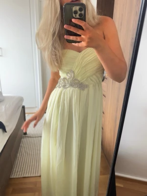 ljusgul Balklänning/ långklänning med pärldetaljer - Elegant ljusgul långklänning/ balklänning med axelbandslös design (bandeau) och vackra stendetaljer i midjan. Klänningen har draperad överdel och en slits framtill som ger en snygg touch. Aldrig använd med lapparna kvar. Strlk 34💛💛💛