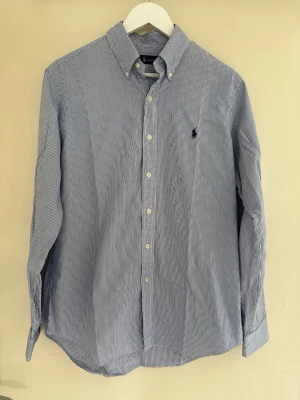 Blårandig Ralph Lauren skjorta  - Tja! Säljer nu denna klassiska blårandiga Ralph Lauren skjortan. Skjortan har button-down krage vilket gör den perfekt att ha under en tröja eller så som jag har på sista bilden. Går både att klä upp och ner beroende på tillfället, dessutom väldigt bekväm! | Storlek: M (passar även L) | Skick: 9/10 | Ärmlängd: 76 cm | Axelbredd: 45 cm | Meddela gärna vid eventuella frågor! Mvh ResellGarms