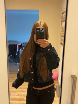 Mörkblå croppad jeansjacka S - Snygg mörkblå croppad jeansjacka med klassisk krage och silverfärgade knappar. Jackan har raka ärmar och kontrastsömmar som ger en cool look. Perfekt att slänga över en hoodie eller t-shirt för en avslappnad stil.