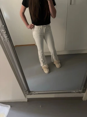 Vita bootcut jeans med fickdetaljer - Säljer ett par vita bootcut jeans med snygga fickor bak och silverknappar. Jeansen har normal midja och är i ett mjukt denimtyg som sitter skönt. Perfekta för dig som vill ha en clean och fräsch look till vardags.