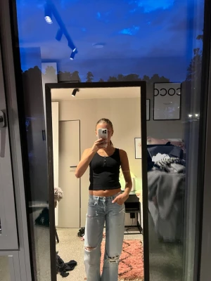Svart ribbad linnetopp med knappar - Snygg svart ribbad linnetopp med tre knappar framtill. Toppen är croppad och ärmlös, perfekt till jeans eller kjol. Enkel och stilren design som passar till många olika looks. Skriv för frågor🩷🫶🏼