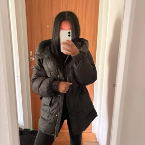 Svart dunjacka från Bershka - Säljer en svart dunjacka från Bershka i storlek XS. Jackan har en oversized passform, stora fickor framtill och dragkedja med knappslå. Perfekt för kalla vinterdagar och riktigt skön att bära. Klassisk design som passar till det mesta.