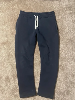 Russemerch byxor  - Säljer ett par mörkblå mjukisbyxor med vita dragsnören i midjan. Byxorna har två sidofickor och är tillverkade i ett mjukt och bekvämt material, perfekt för chill dagar. Passformen är rak och avslappnad.