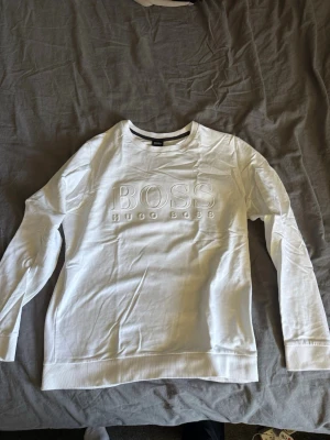Vit sweatshirt från Hugo Boss - Snygg vit sweatshirt från Hugo Boss med broderad logga på bröstet. Tröjan har rund halsringning och långa ärmar. Perfekt för en clean och stilren look.