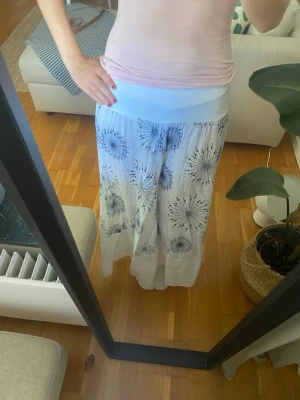Vit långkjol med blått mönster - Säljer en vit lång kjol med blått mönster. Kjolen går ner till fötterna på mig som är 166cm och kommer med tillhörande skärp. 💕