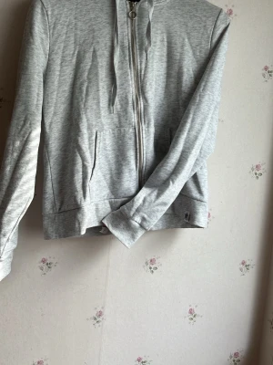 Ljusgrå zip hoodie med fickor och huva - En stilren ljusgrå hoodie med dragkedja framtill och två fickor. Hoodien har långa ärmar, justerbar huva med snören och är tillverkad i mjukt sweatshirtmaterial. Perfekt för en avslappnad look. Det står XL men passar bra som M, går även bra som S för en oversized look.