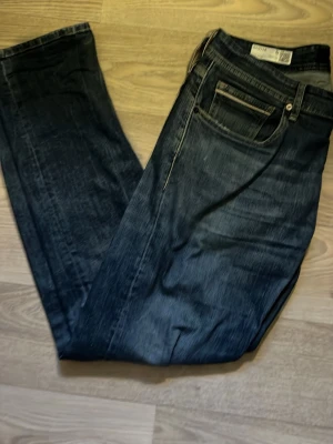 Mörkblå straight fit jeans Grover - Snygga mörkblå jeans från Grover i straight fit-modell. Klassisk femficksdesign och diskret tvättad look. Perfekta för dig som gillar en enkel och stilren stil. Tillverkade i slitstarkt denimtyg. Midjemått- 44cm ytterbenslängd- 100cm
