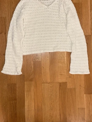 Vit virkad stickad tröja - Säljer en vit stickad tröja med virkat mönster och v-ringning. Tröjan har långa ärmar och är något kortare i modellen. Perfekt för lager på lager och ger en fräsch look till din outfit.