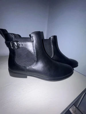 svarat ecco Chelseaboots - Dress Classic 15 chelseaboots från ECCO är ett utmärkt val för stilmedvetna. I svart skinn med elastikpaneler och en dekorativ rem med spänne på utsidan, erbjuder dessa boots både design och funktion. Uttagbara innersulor och ECCO Fluidform-teknologi ger en lättviktssula som ger överlägsen komfort. Helt oanvända. Orginal pris 1600kr. Skickar snabbat och pris är inte hugget i sten. Storlek 42