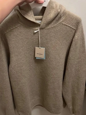 Beige hoodie från Gran Sasso - Mysig beige hoodie från Gran Sasso i mjukt stickat material. Tröjan har huva, långa ärmar och ribbade muddar vid ärmslut och nederkant. Perfekt för en avslappnad och stilren look.