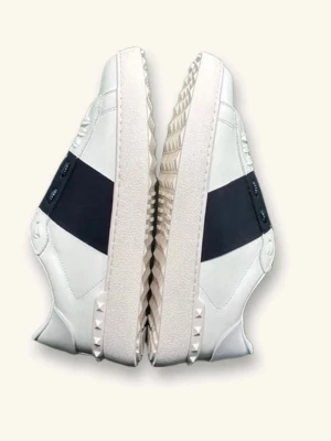 Vita sneakers med svart detalj - Snygga vita sneakers med bred svart rem över sidan och coola nitar på sulan. Skorna har en chunky sula med mönstrad kant och svarta snören. Perfekta för dig som vill ha en stilren men edgy look.