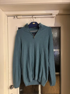 Blå stickad tröja med halv dragkedja - Snygg blå stickad tröja med halv dragkedja och hög krage. Tröjan har långa ärmar och ribbade muddar vid ärmslut och nederkant. Perfekt för lager på lager och enkel att matcha med jeans eller chinos.