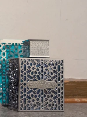 Sälj/ byte Rayhaan Aquatica  - Unik parfymflaska med namnet Rayhaan, designad i en fyrkantig form med detaljerat orientaliskt metallmönster i silver. Flaskan är genomskinlig med blå inslag och har ett matchande dekorativt lock. Perfekt för dig som gillar exklusiv och stilren design.
