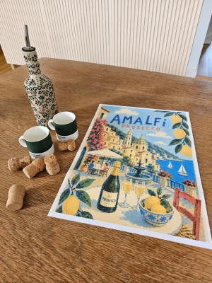 Amalfi Prosecco A3 poster  - Snygg poster med Amalfi Prosecco-motiv i färgerna blått, gult och grönt. Motivet visar en italiensk kuststad med citroner, proseccoflaska och glas, samt segelbåtar och terrass. Perfekt för dig som gillar retroinspirerad konst och vill ha semesterkänsla hemma.