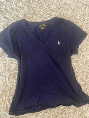 Mörkblå v-ringad t-shirt Polo Ralph Lauren - Snygg mörkblå t-shirt från Polo Ralph Lauren med v-ringning och klassisk logga broderad på bröstet. Tillverkad i mjuk bomull och har korta ärmar. Perfekt för en avslappnad och stilren look.