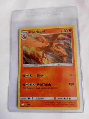 Charizard Pokémonkort 5/18 - Säljer ett Charizard Pokémonkort med eldig orange bakgrund och illustration av Charizard. Kortet har 180 HP och attacker som Slash och Wild Tackle. Det är inplastat i ett Ultra Pro-skydd och har samlarnummer 5/18. Levereras i plastficka. Pris kan diskuteras🙌. Mvh Rasmus.